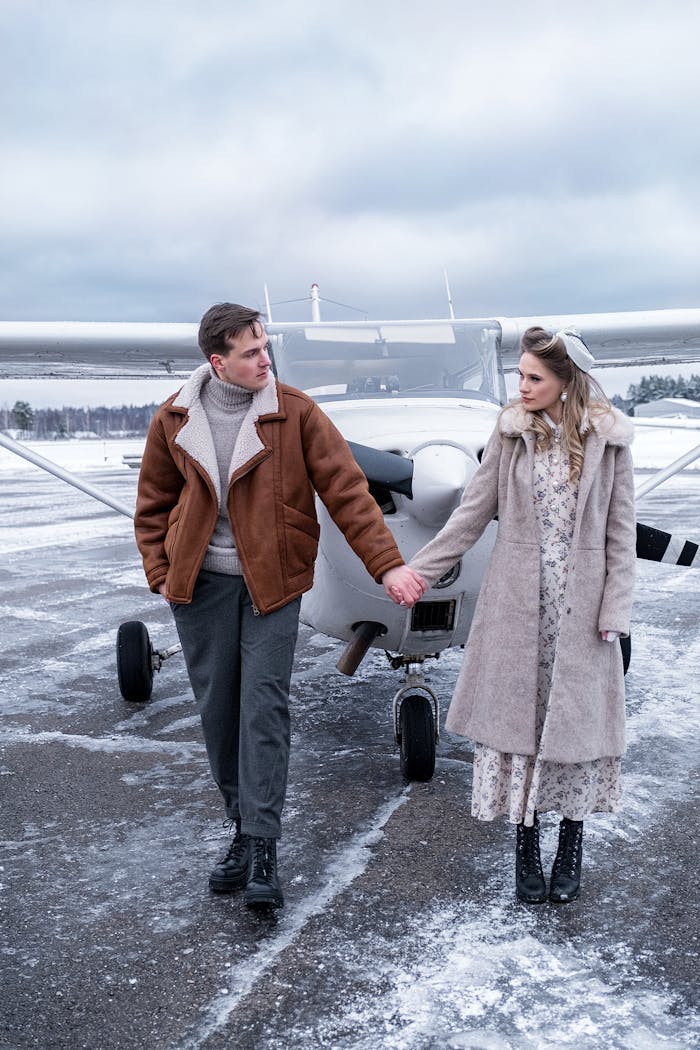 Couple holding hands near an airplane on a snowy airfield, capturing romantic winter travel vibes.